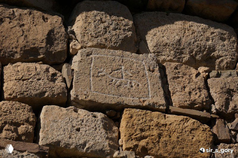 Крупный план прямоугольной плиты с древними знаками или надписью, встроенной в стену храма Тхаба-Ерды; структура камня и швы кладки видны явно.