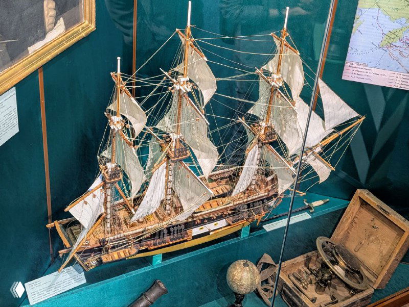 Макет парусного судна и морские артефакты в витрине музея Каргополя: модель корабля, глобус и навигационные предметы экспозиции.