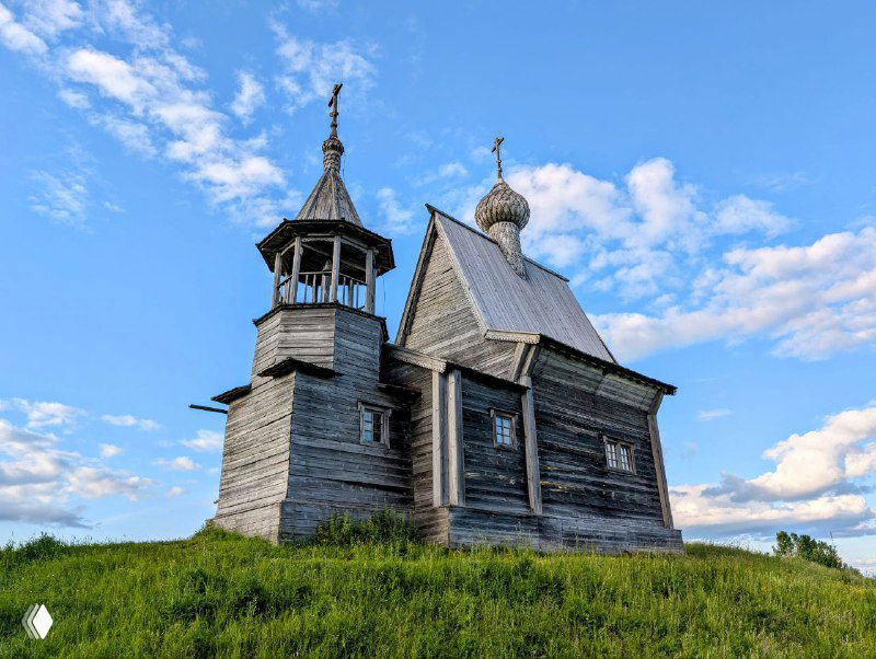 Купол и колокольня Никольской часовни крупным планом: резная деревянная архитектура на фоне ясного голубого летнего неба