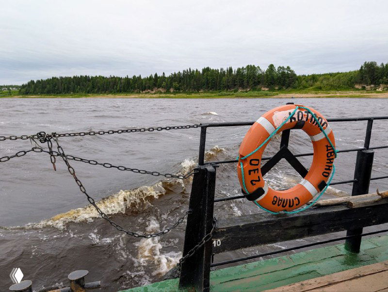 Спасательный круг на ограждении парома на фоне бурной воды Северной Двины и волнообразного течения у берегов Курострова.