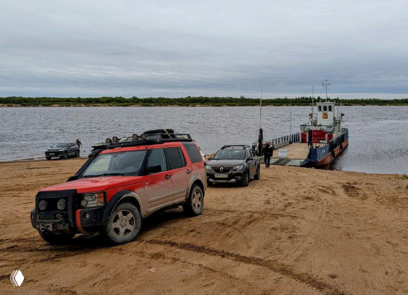 Общий план берега и пристани: несколько автомобилей выстраиваются в очередь на посадку, паром пришвартован у песчаного косогора на Курострове.