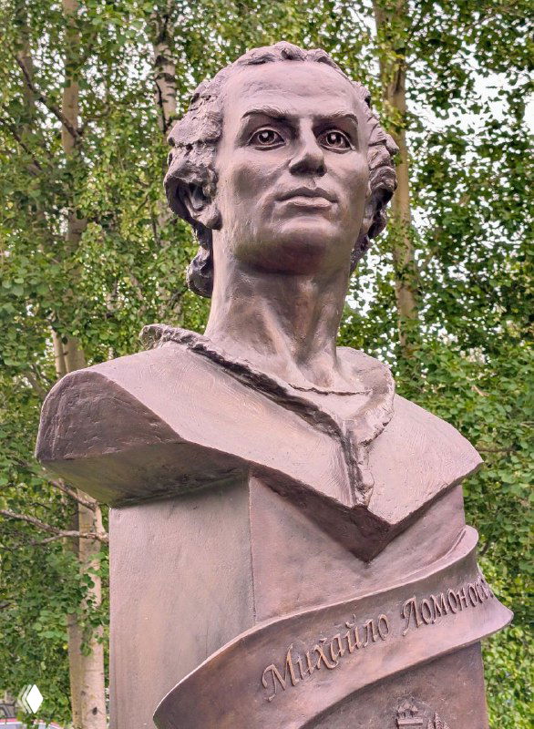Бюст Михаила Ломоносова на фоне зелёных берёз рядом с дорогой к музею в Ломоносово, памятник вблизи главного села на Курострове.