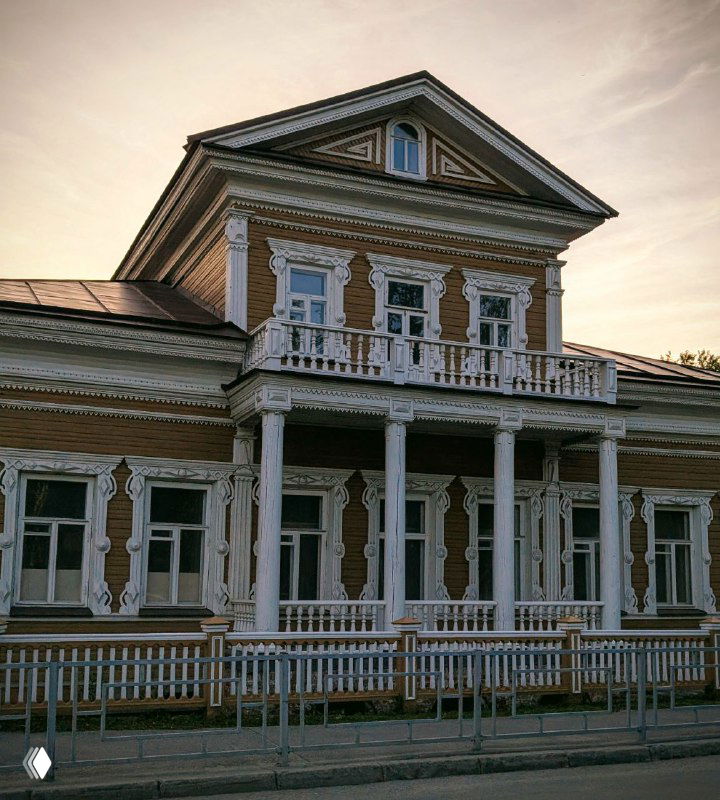 Фасад старинного деревянного дома в Вологде с резным кружевным декором вокруг окон и большим угловым балконом над крыльцом, вечерняя подсветка