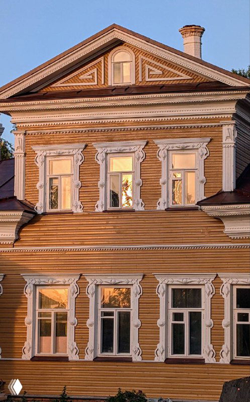 Фрагмент фасада деревянного дома в Вологде с декорированными наличниками и орнаментом, отражающимся в тёплом закатном свете на стеклах