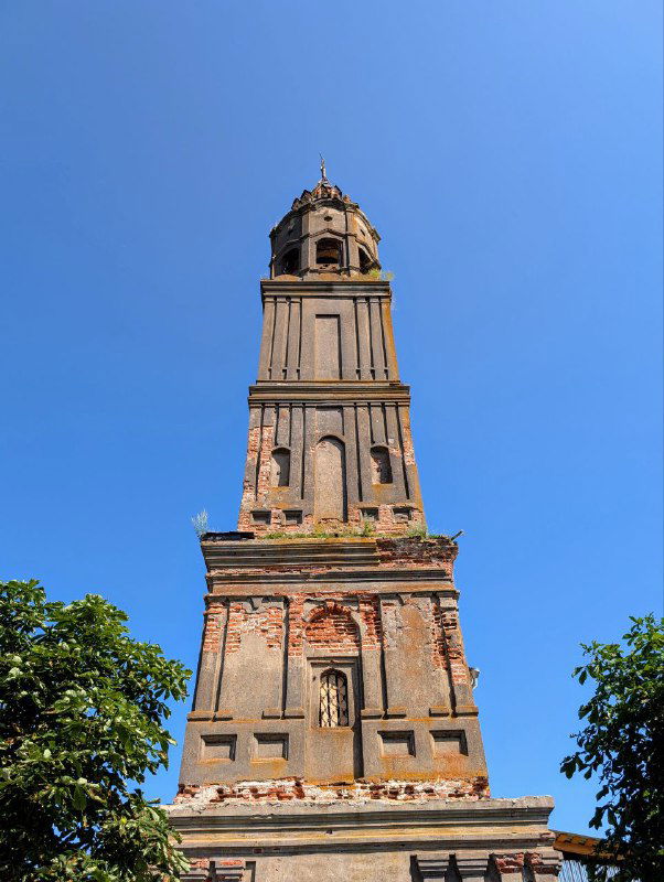 Строгий вертикальный кадр колокольни Воскресенской церкви — слои штукатурки и оголённый кирпич создают фактуру старения здания.