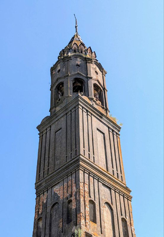 Крупный план верхней части колокольни с декоративными элементами барочного характера и частично сохранёнными оконными проёмами.