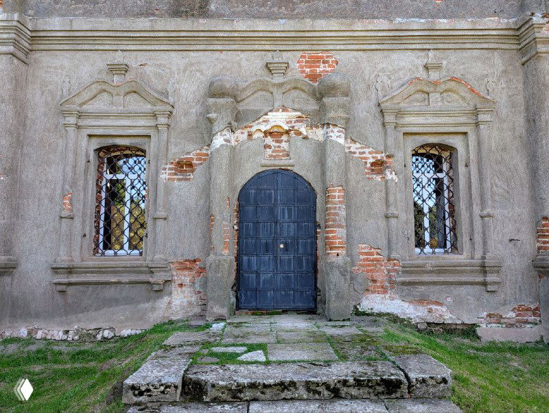 Входная часть Воскресенской церкви: тяжёлые деревянные двери в обветшалом портале, видны растрескавшиеся слои штукатурки и кирпича.