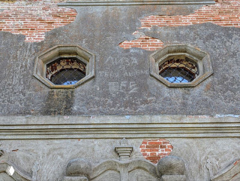 Фрагмент фасада с небольшими оконцами в восьмиугольных проёмах и едва читаемыми надписями на старой штукатурке рядом с растрескавшимся кирпичом.
