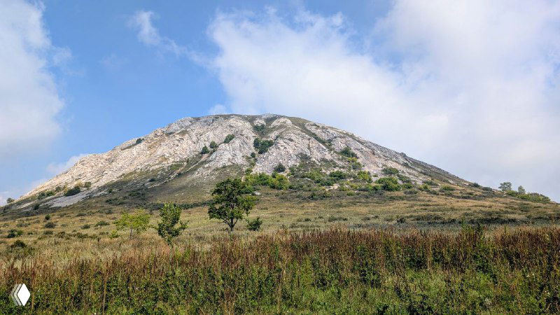 Крупный план шихана с обнажёнными известняковыми откосами, зелёные подножия и чистое голубое небо без людей в кадре.