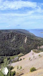 Вид с высокой точки на обширную лесистую излучину Волги в пределах нацпарка «Самарская лука», с голубым небом и рекой на горизонте, панорама.