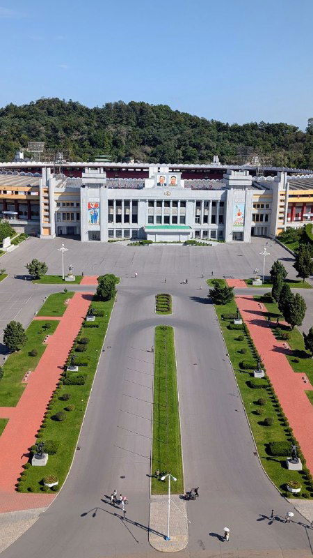 Вид с высоты: парадная аллея и административные здания перед аркой, аккуратные дорожки и симметричная озеленённая композиция внизу.