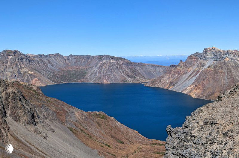 Широкий план кратерного озера Чон: гладкая водная поверхность тёмно-голубого цвета и береговые обрывы Пэкту.