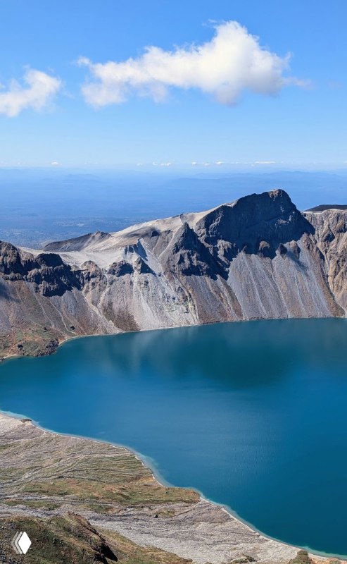 Вид сверху на изумрудную воду Чон и крутые склоны Пэкту; на горизонте виднеется плоская равнина за горным кольцом.