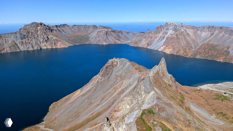 Панорама гребня и острого мыса в центре кратера, окружённого тёмной водой озера Чон и стенами вулканического кратера.