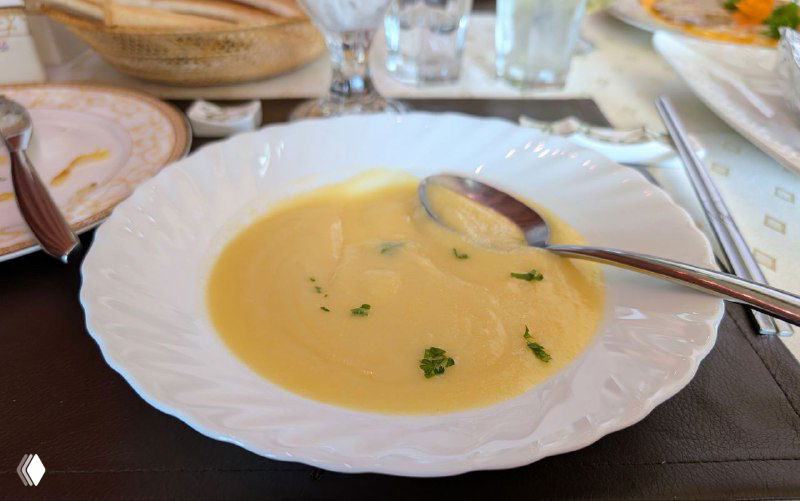 Кремовый картофельный суп в белой глубокой тарелке, ложка внутри, украшение зеленью, ресторанный стол и салфетка.