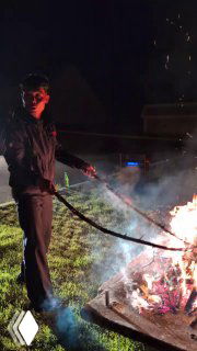 Ночной пикник: мужчина у большого костра, в фоновой подсветке фары автобуса, атмосфера вечерней вылазки и музыки.