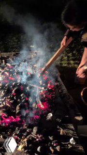 Человек разравнивает угли и раскладывает горячие угли после костра, рядом видны остающиеся угли и посуда — сцена пикника.