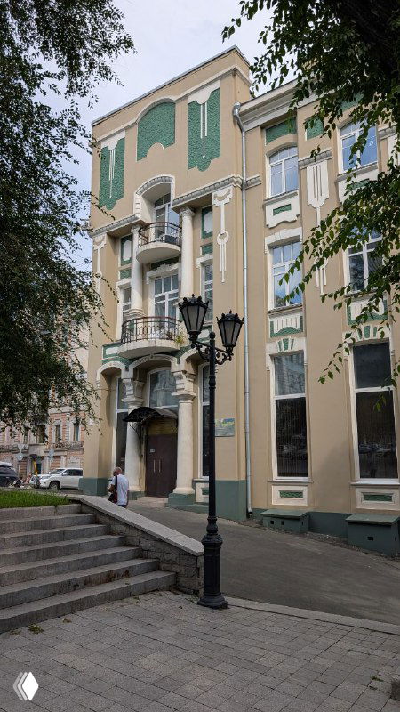 Пастельно-окрашенный жилой дом во Владивостоке с декоративными фасадными элементами и уличными фонарями, дневной снимок фасада.