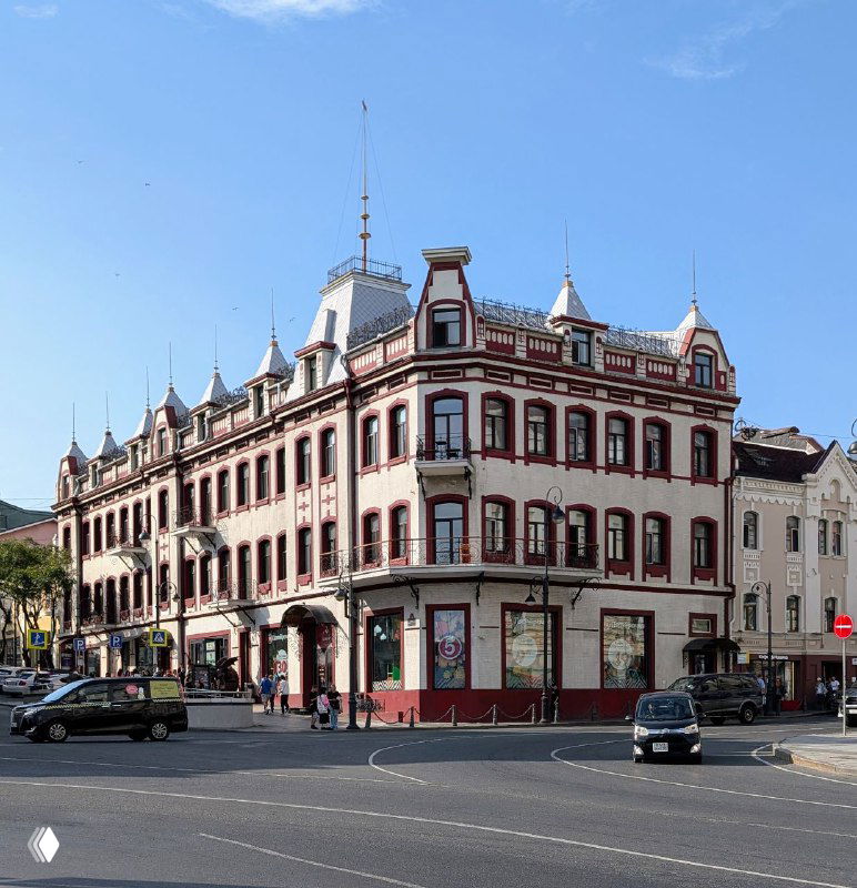 Угловой исторический дом на перекрёстке Владивостока с богатой архитектурной деталировкой, просторная площадь перед фасадом и городской фон.