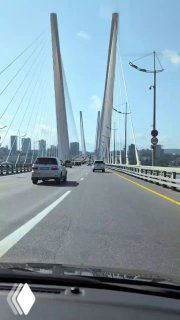 Вид с проезжей части на пилоны и тросы вантового моста: ракурс с дороги показывает конструктивные элементы и городской горизонт.