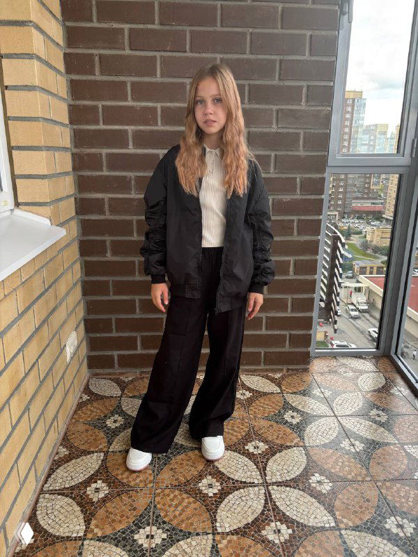 Девочка около 12 лет стоит на балконе в школьной одежде и кроссовках; фото иллюстрирует детей как активных онлайн-покупателей поколения Альфа.