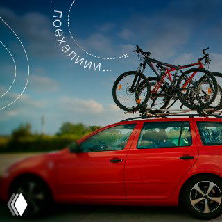 Красный автомобиль с багажником на крыше, на котором закреплены велосипеды; размытый фон дороги и неба, фотография для анонса велосезона в Москве.