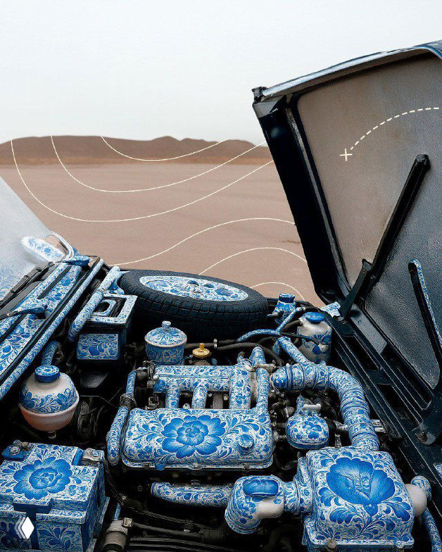 Крупный план моторного отсека автомобиля, элементы двигателя и детали покрыты бело‑синим гжельным орнаментом, декоративная роспись на технических частях.