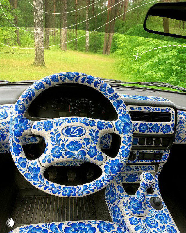 Салон автомобиля: руль, торпеда и элементы управления расписаны в бело‑синием гжельном стиле; детализация узора заметна в интерьере.