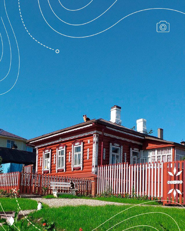 Красный купеческий дом с резными наличниками и белым забором на зеленом газоне — исторический жилой дом в Тарусе.