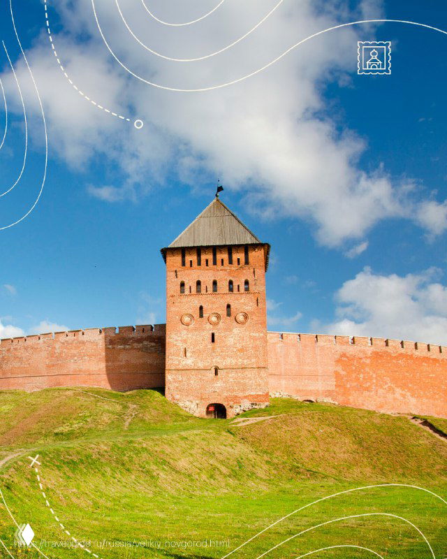 Крупный план высокой кирпичной оборонительной башни Детинца в Великом Новгороде на фоне чистого голубого неба и зелёного склона у стен крепости.