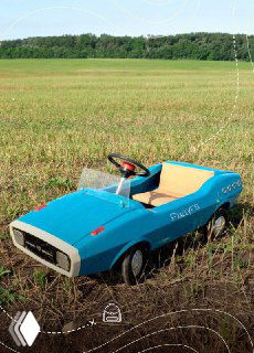 Голубой педальный родстер стоит в поле на фоне леса; фотосъёмка на открытом воздухе создаёт ностальгическое настроение путешествия.