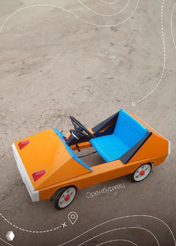 Ярко‑оранжево‑голубая педальная машина с просторным салоном, фото крупным планом на сером фоне; видно простую конструкцию и цветовую гамму.