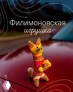 Крупный план филимоновской керамической игрушки в яркой традиционной росписи, стоящей на капоте автомобиля на фоне дороги и природы.