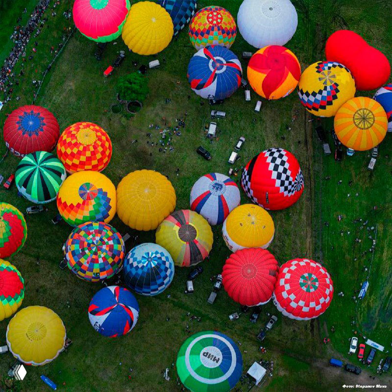 Плотная группа разноцветных воздушных шаров на земле в ожидании подъёма; фотографии с высоты демонстрируют геометрию их расположения.