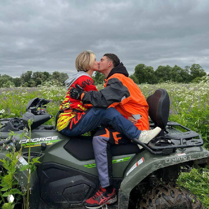 Пара целуется, сидя на стоящем в цветущем поле квадроцикле во время романтического тура на открытом воздухе рядом с Подмосковьем.