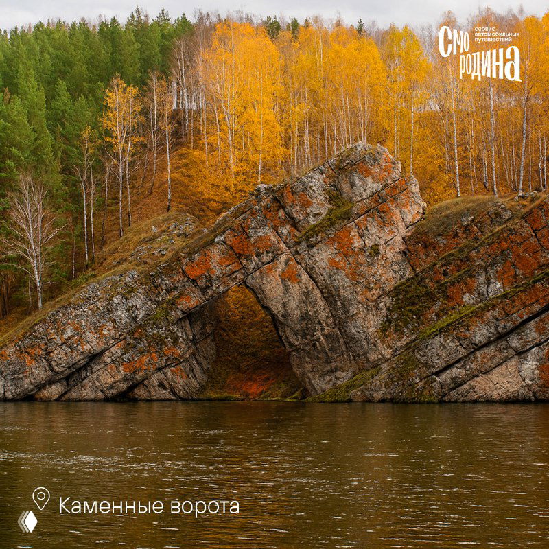 Каменная арка над рекой на фоне смешанного леса: крупный план скального образования у воды и зелёно-жёлтые деревья.