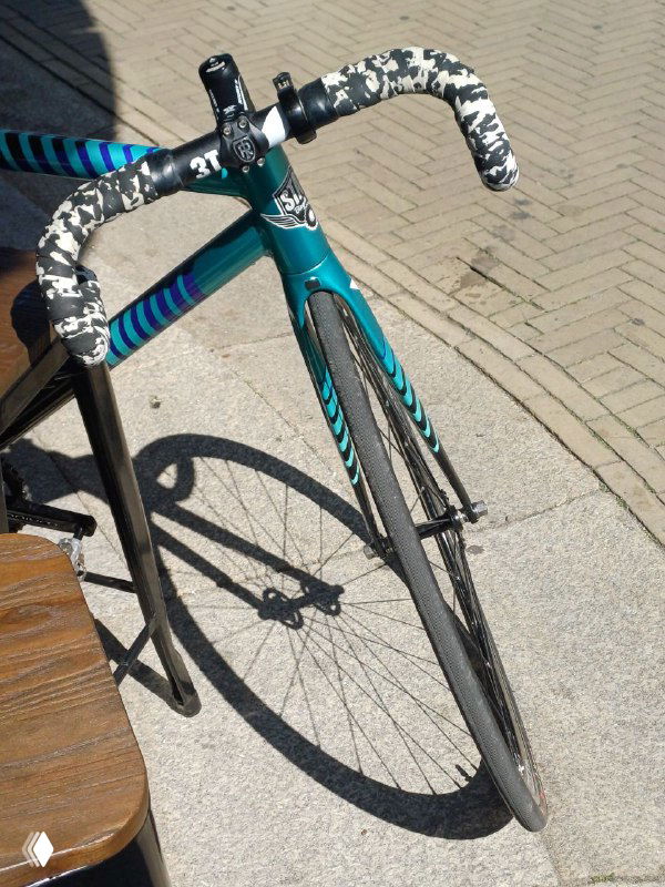 Крупный план рулевой колоды и переднего колеса трека Undefeated — видна карбоновая вилка, оформление обмотки и дорожное покрытие рядом.