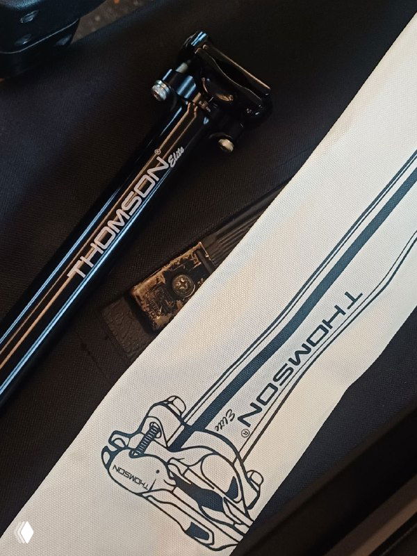 Крупный план алюминиевого подсидельного штыря Thomson Elite и упаковки — видна маркировка и текстура изделия на фоне чехла и аксессуаров.