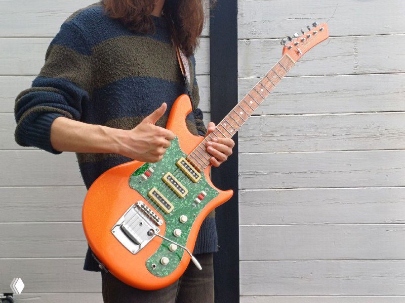 Человек держит яркую электрогитару — кадр иллюстрирует отреставрированный советский инструмент Урал 650, готовый к игре и передачи новому владельцу.