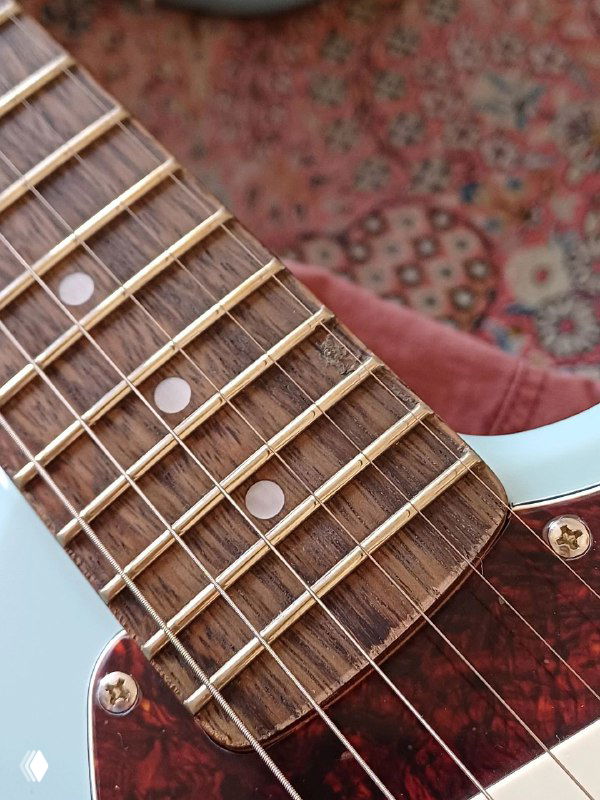 Крупный кадр грифа Squier Mustang: изношенные и кривые лады, потертости вокруг ладов и следы ремонта на накладке.