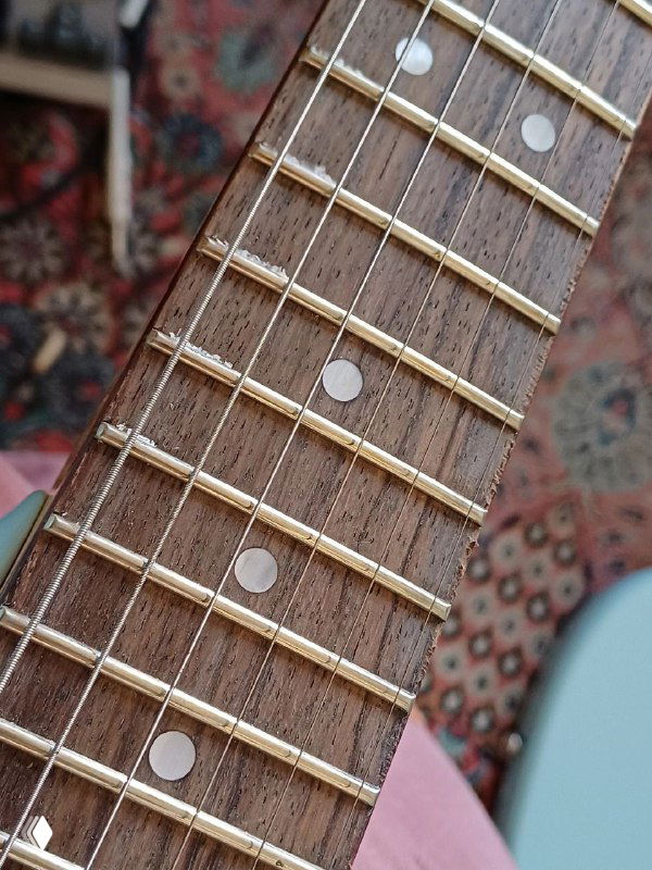 Детальный снимок накладки грифа Squier Mustang: пятна, царапины и неровности ладов, указывающие на дефекты качества.