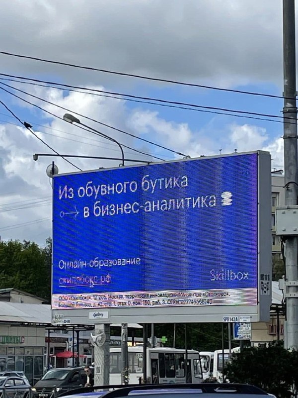 Фото городского рекламного билборда с надписью о переходе в бизнес-аналитику; видны столбы, провода и пасмурное небо.