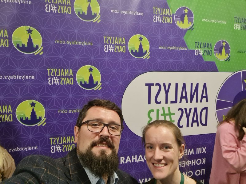 Селфи с участниками конференции у брендированной стены Analyst Days: несколько людей улыбаются, видна часть логотипа и оформление задника.
