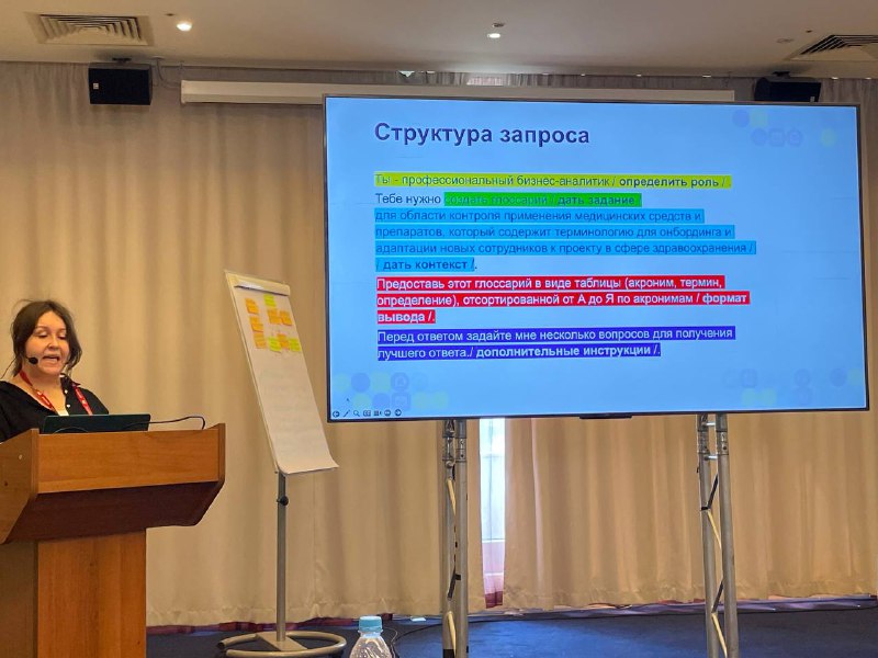 Лектор у трибуны в конференц-зале, рядом большой экран со слайдом «Структура запроса», флипчарт и занавеси.