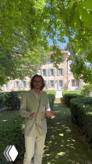 Человек в светлом костюме в тенистом саду на фоне загородного дома — кадр как референс для lifestyle‑видео недвижимости и премиальных обзоров.