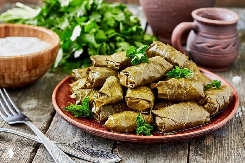 Тарелка с долмой на деревянном столе, рядом зелень и столовые приборы; фото служит визуальной метафорой пропорций и ингредиентов в тексте про бюджет