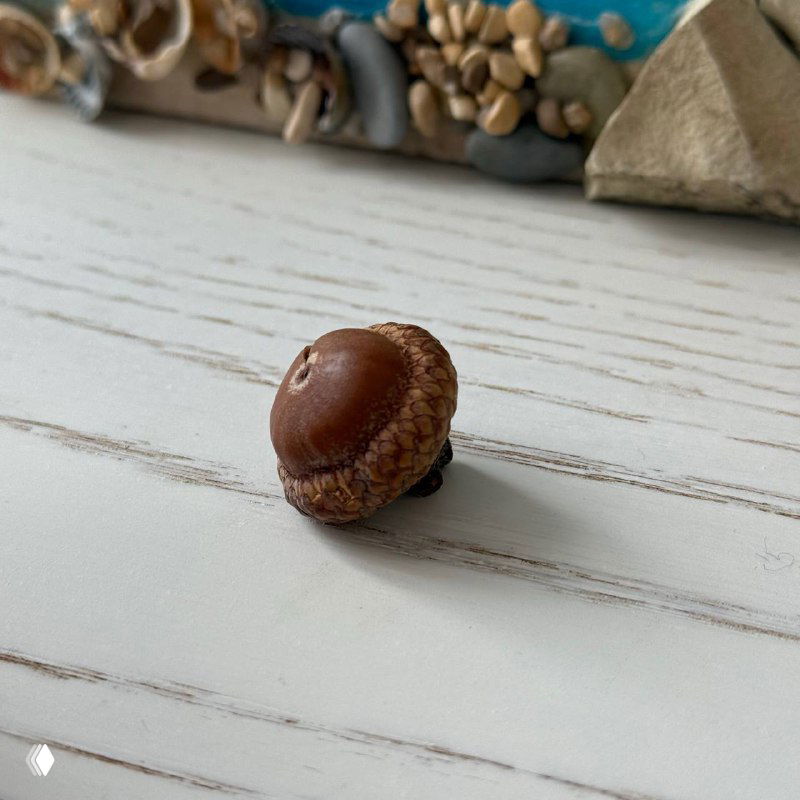 Крупный план желудя на светлой деревянной поверхности; акцент на текстуре шляпки и натуральном фоне, метафора небольшого долгосрочного актива или идеи.