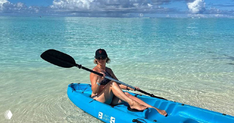 Автор поста сидит в синем каяке на мелководье Мальдив: шляпа, солнечные очки, прозрачная бирюзовая вода и облачное небо на заднем плане.