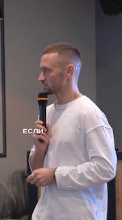 Мужчина с микрофоном в белой толстовке на сцене, кадр крупным планом — иллюстрация мысли о пластиковых картах и альтернативах.