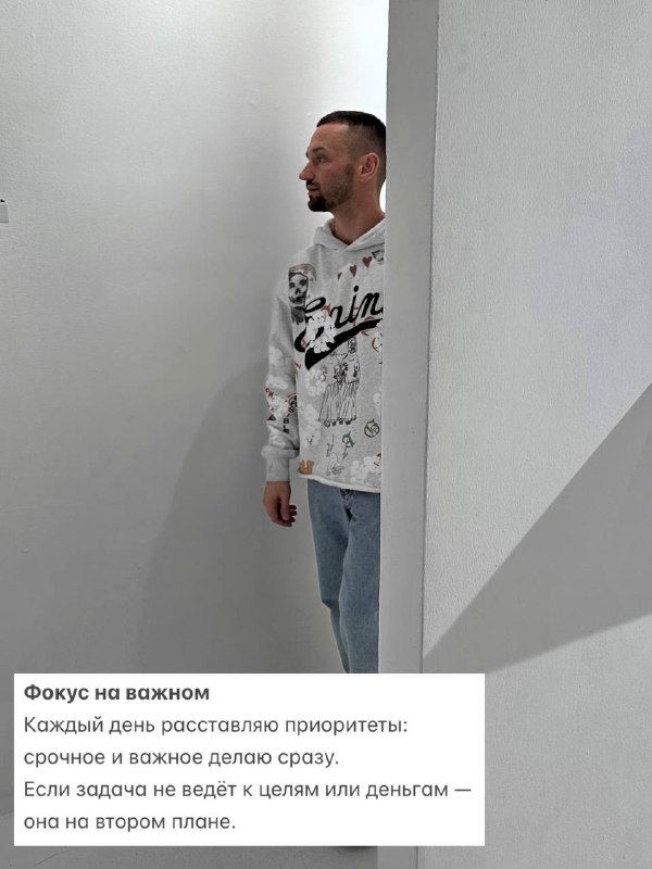 Мужчина стоит у светлой стены в просторном помещении, смотрит в сторону; изображение символизирует фокус на важном и расстановку приоритетов в ежедневной жизни.